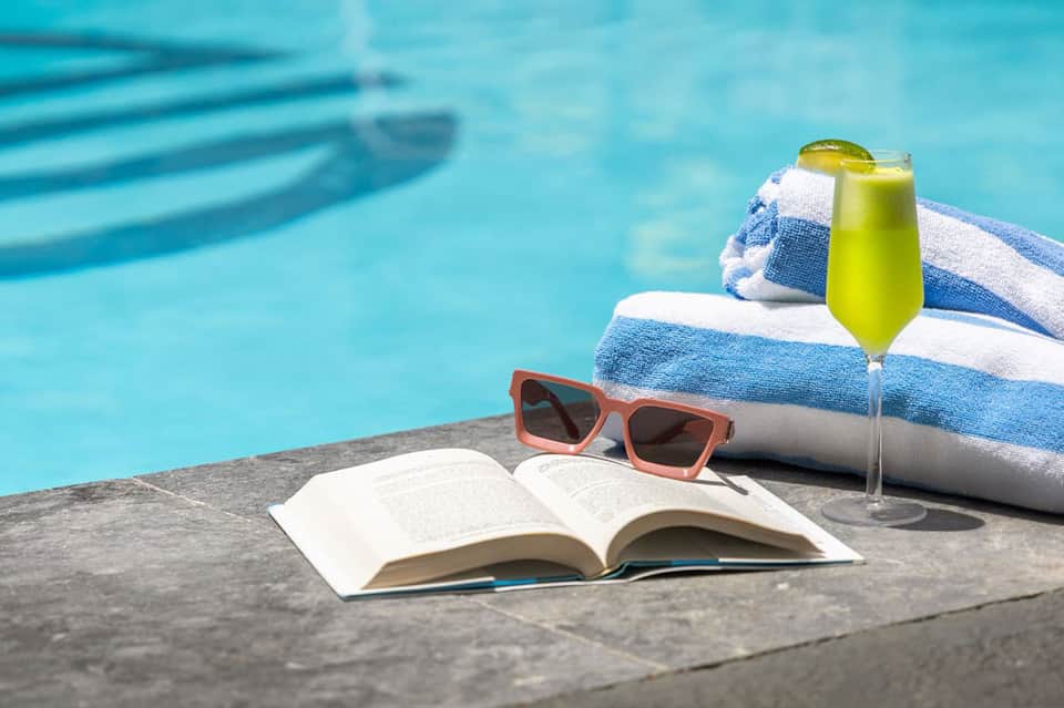 Poolside scene with open book, sunglasses, towel, and lime-green cocktail