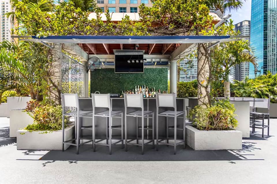 Rooftop bar with pergola, greenery, and seating along waterfront cityscape