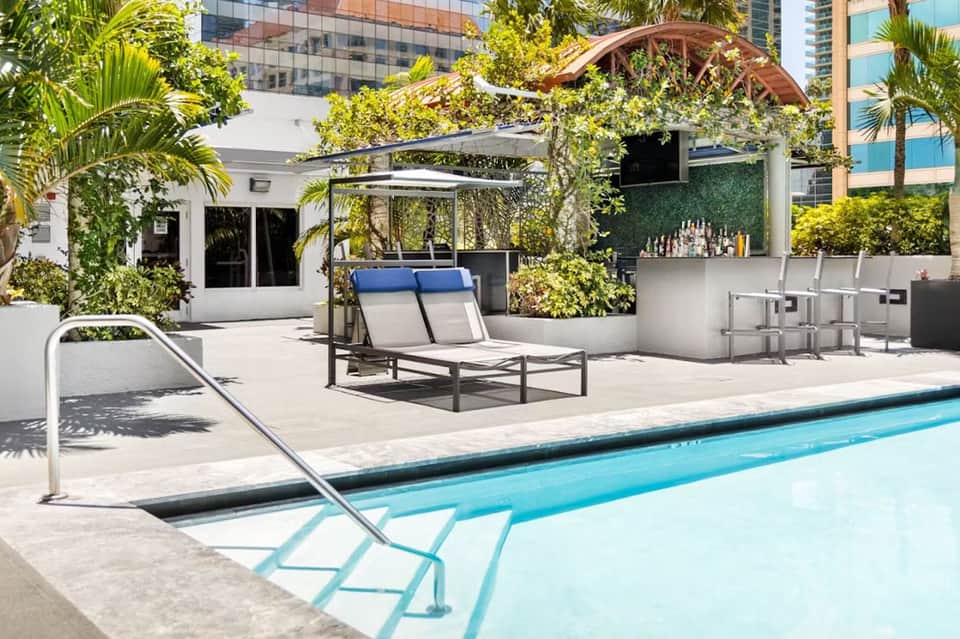 Modern rooftop pool with lounge chairs, green landscaping, and city views