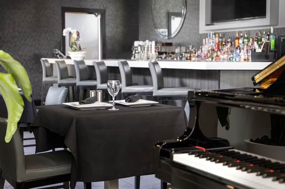 Upscale bar and lounge with piano, bar seating, dark modern décor, and ambient lighting
