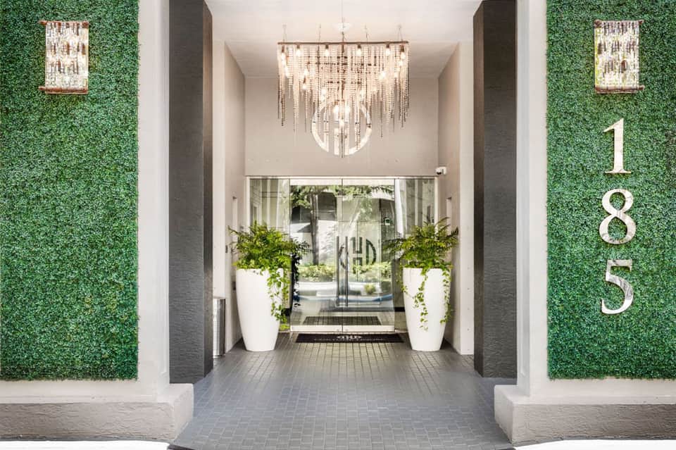 Modern building entrance with green living walls, elegant chandelier, and white planter urns
