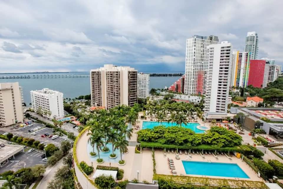 Aerial view of beachfront resort with multiple pools, palm trees, high-rise towers, and ocean backdrop