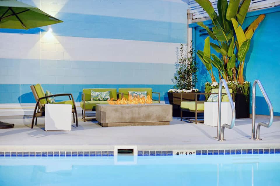 Resort poolside patio with blue striped walls, lounge chairs, fire pit, and tropical plants