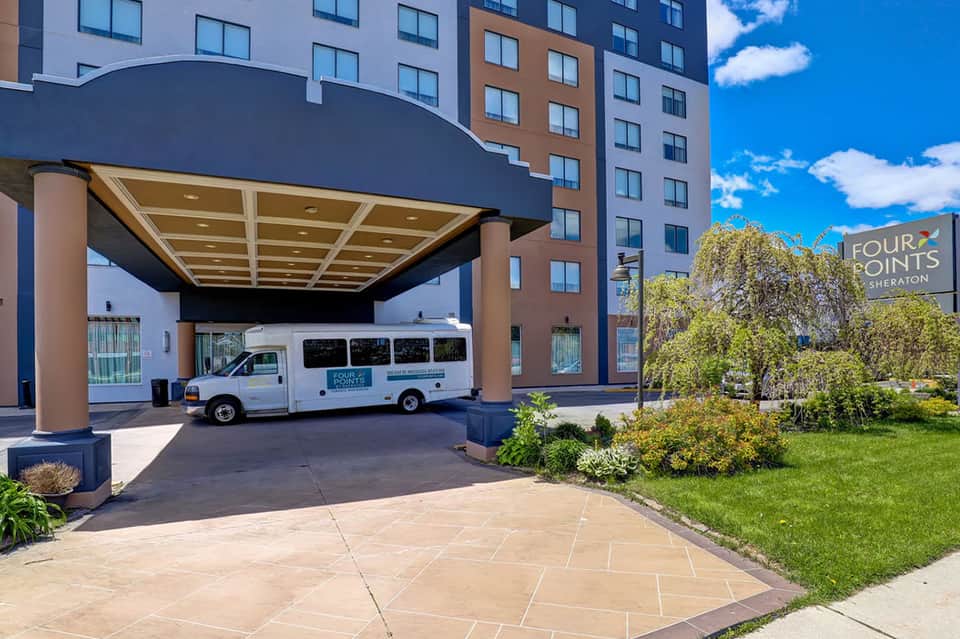Hotel entrance with modern building, shuttle van, and landscaped grounds