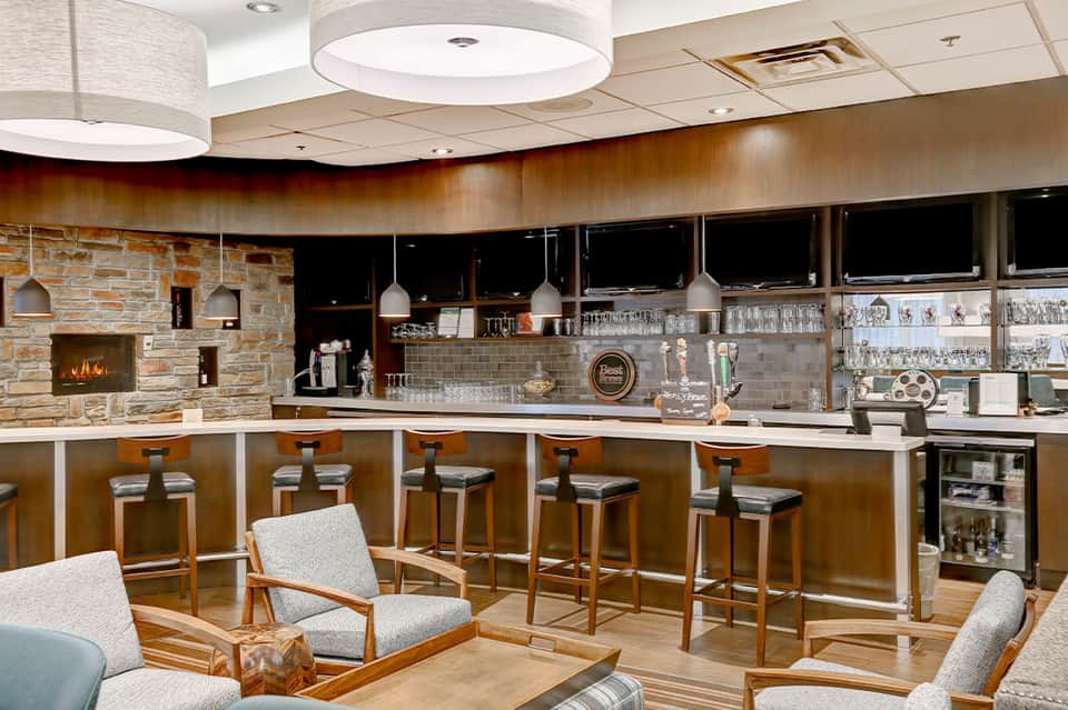 Hotel bar lounge with stone fireplace, pendant lighting, bar seating, and ambient wood finishes