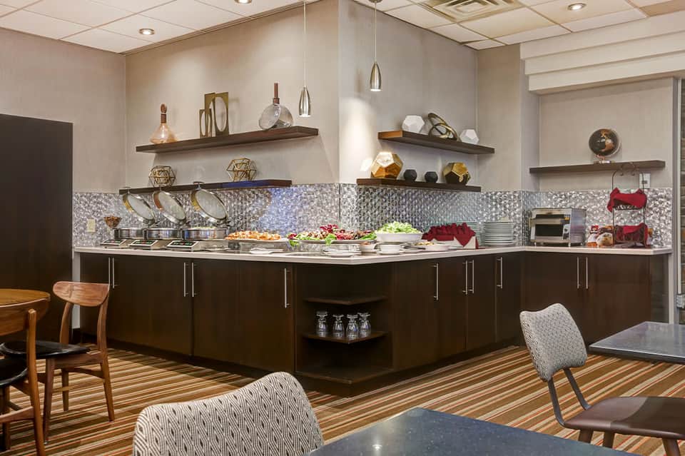Elegant hotel kitchen display with dark cabinetry, silver cookware, pendant lights, and decorative shelving