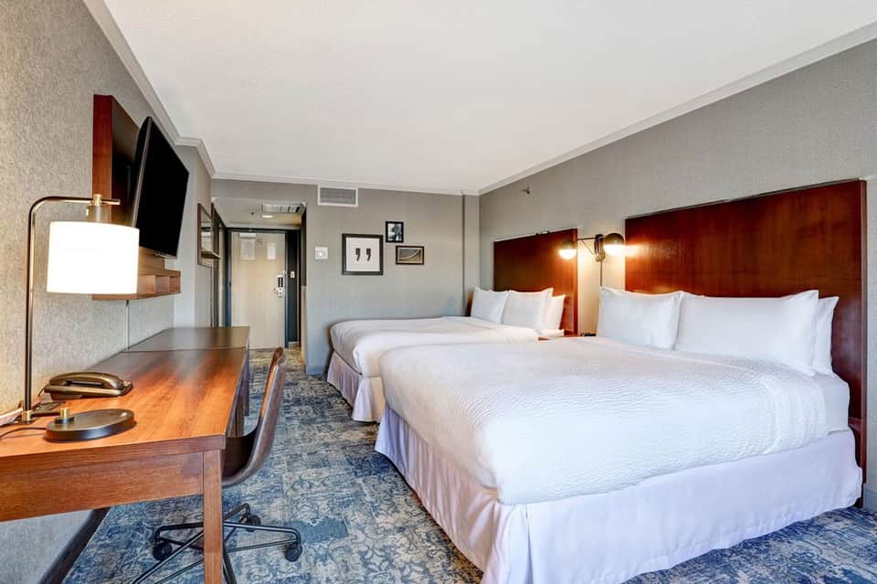Hotel room with two queen beds, wood headboards, desk, flat-screen TV, and modern décor