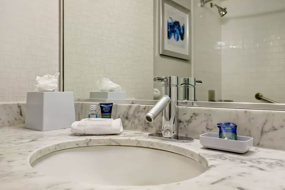 Marble bathroom vanity with circular sink, chrome faucet, mirror, and white toiletries