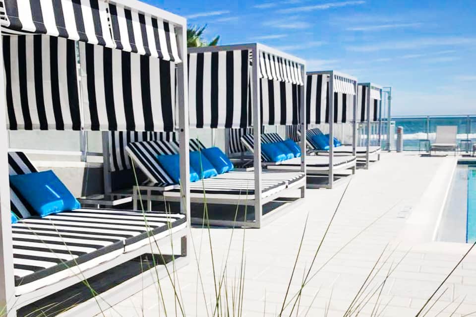 Row of striped beach cabanas with blue cushions and white frames along a sunny coastal deck