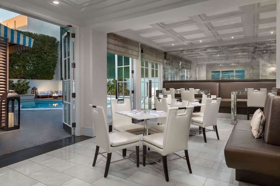 Modern restaurant dining room with white chairs, tables, pool view through glass doors, and contemporary design