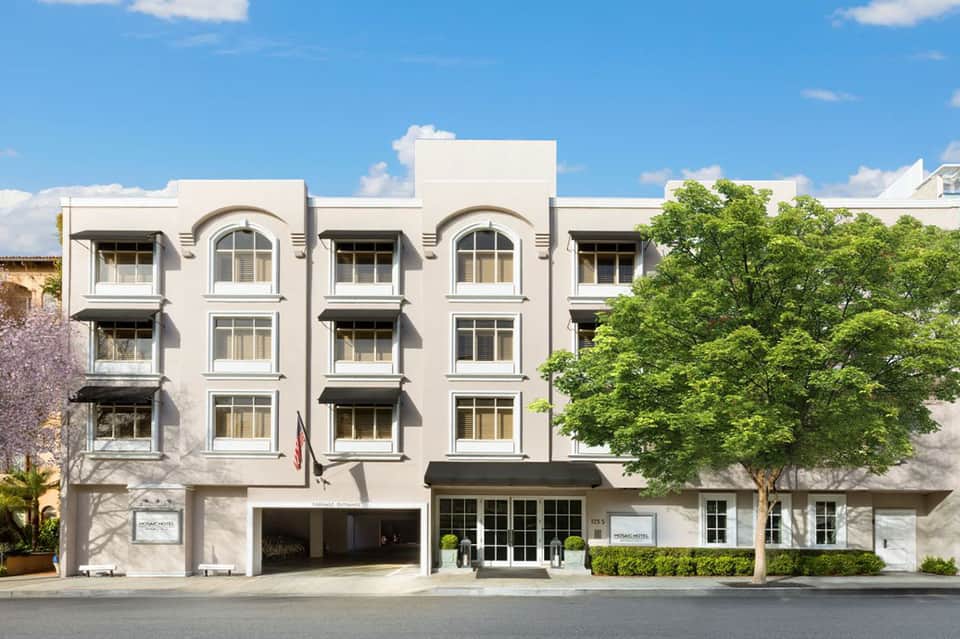 Modern white hotel exterior with arched windows and lush green foliage