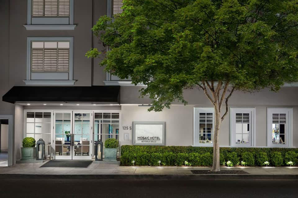 Mosaic Hotel storefront with clean modern facade, black awning, glass doors, landscaped hedges, and street-level entrance