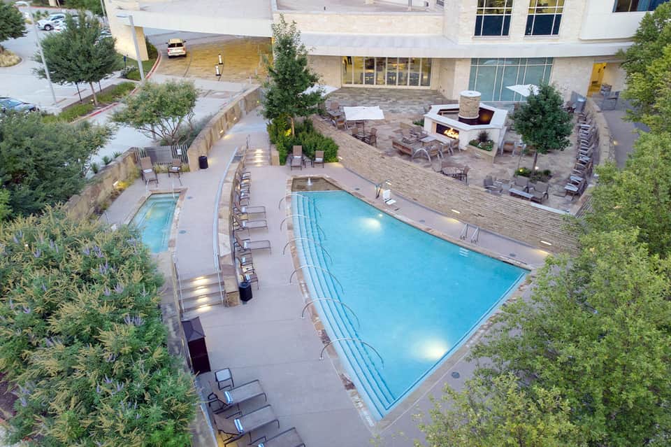 Aerial view of resort pool complex with fireplace seating area, spa, landscaping and multiple outdoor spaces