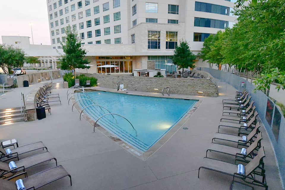 Urban rooftop hotel pool surrounded by modern high-rise buildings and green landscaping