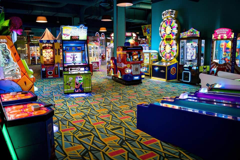 Colorful arcade game room filled with illuminated gaming machines, bright patterns on flooring, and entertainment cabinets under dark ceiling