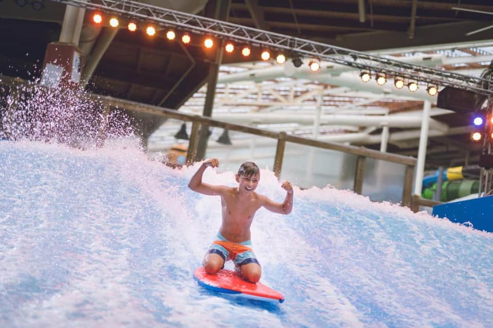 Child surfing on indoor wave pool with foam wave and professional lighting in facility