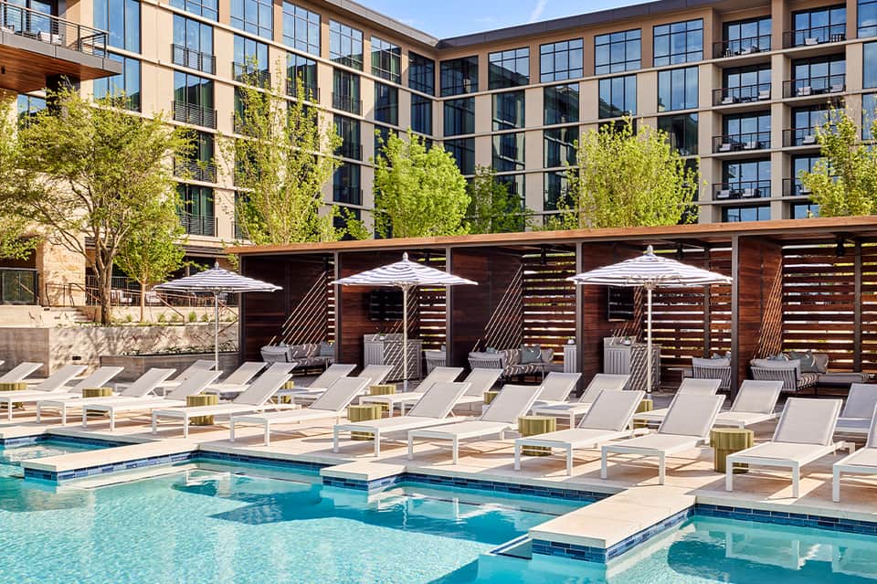 Contemporary courtyard pool with white lounge chairs, umbrellas, and multi-story apartment building