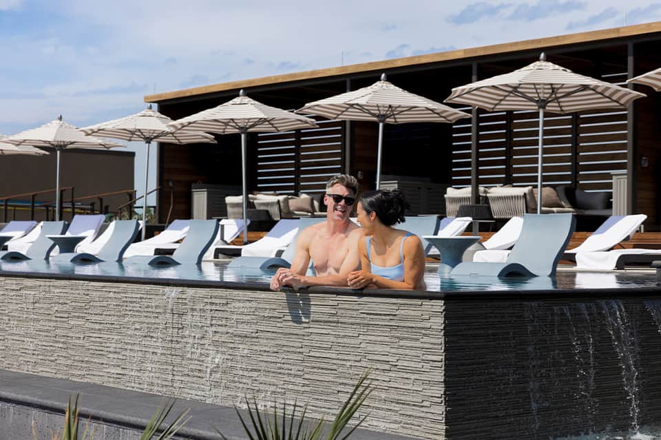 Couple enjoying infinity pool with white lounge chairs and umbrellas in background