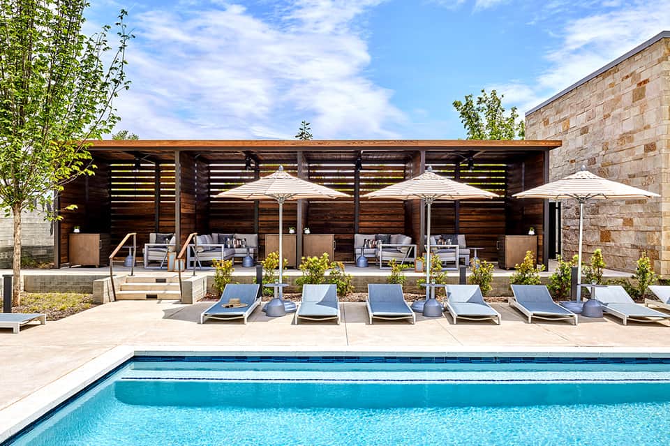 Resort pool area with modern wood pergola, white umbrellas, and lounge seating