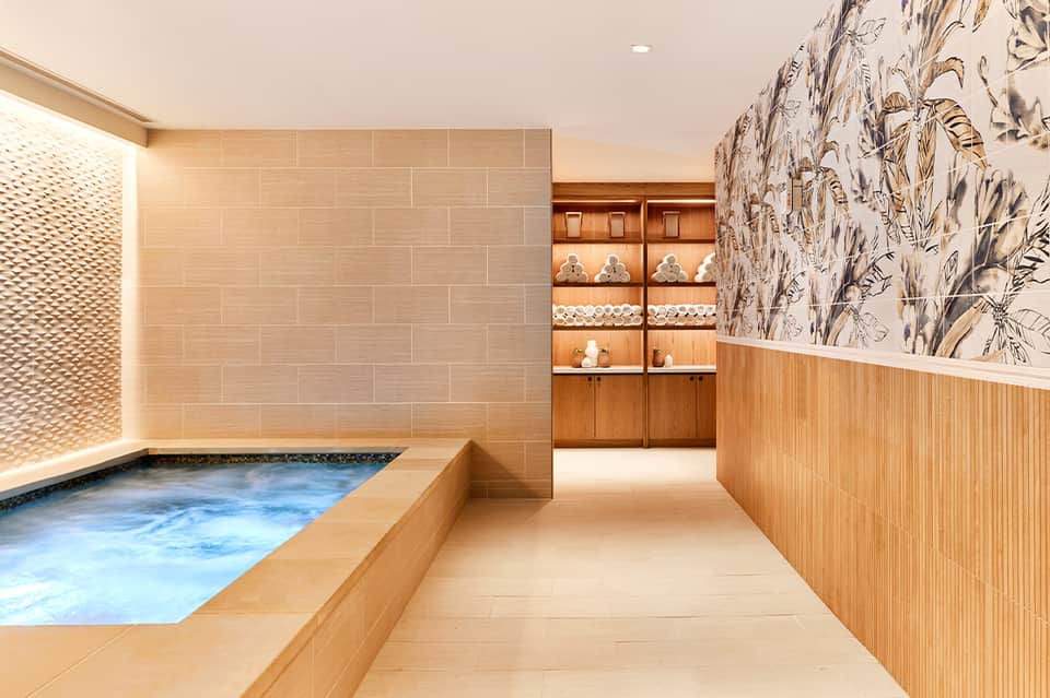 Luxury indoor spa pool with warm water, beige tiles, and wooden accents