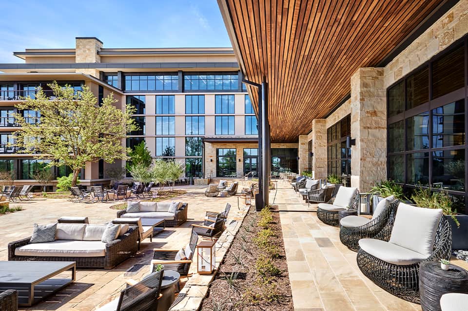Modern resort courtyard with stone patio, contemporary seating areas, wooden ceiling detail, and multi-story building
