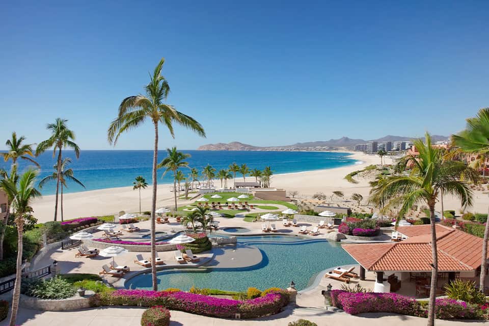 Beachfront resort with curved pool overlooking sandy beach, ocean, and distant mountains