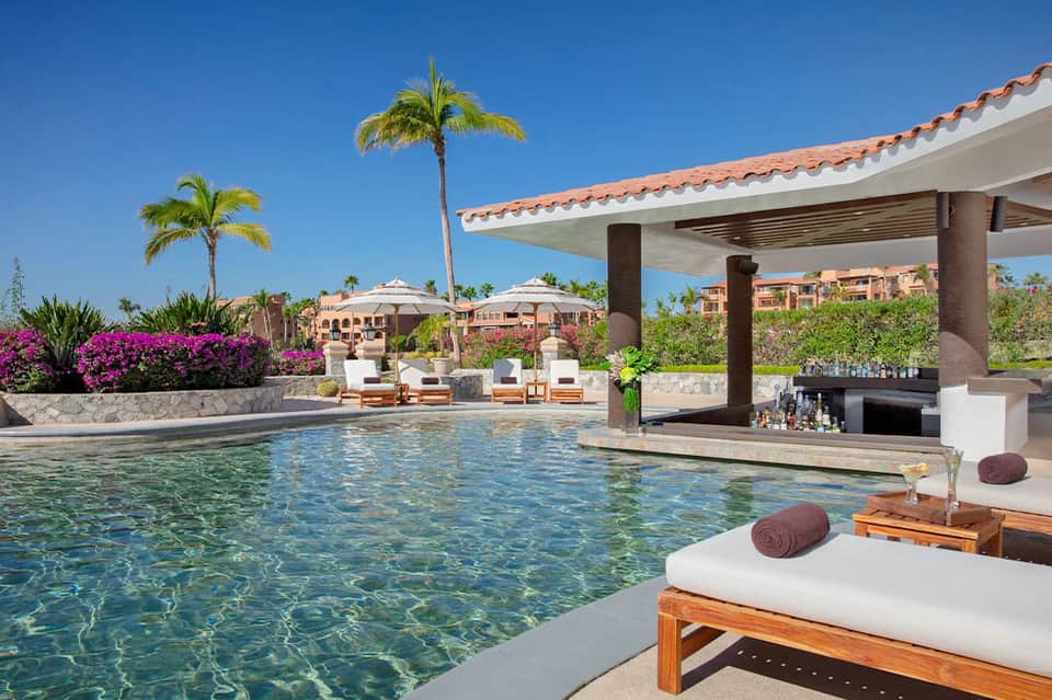 Luxury resort pool with crystal clear water, cabanas, palm trees, magenta bougainvillea, and mountain views