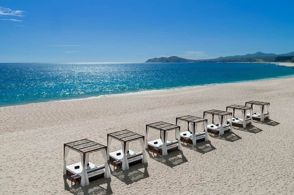 Row of white beach cabanas with black canopies on pristine sand overlooking turquoise ocean