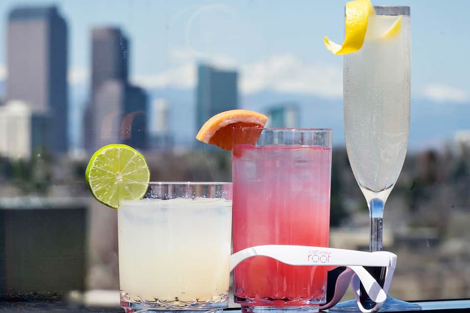 Three cocktails with citrus garnishes against a blurred cityscape backdrop