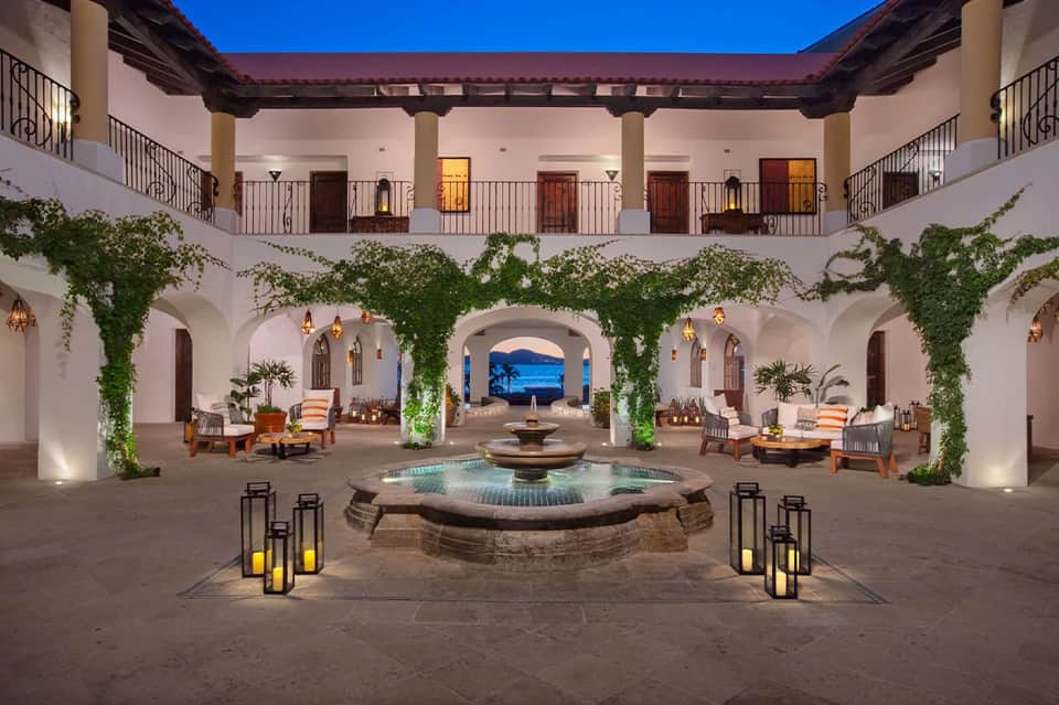 Spanish colonial courtyard at dusk with central fountain, ivy-draped columns, and ocean view arch