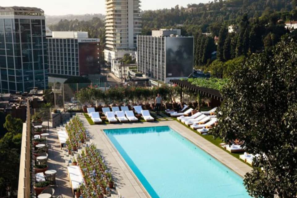 Urban rooftop pool deck with blue loungers overlooking downtown skyline and forested hills