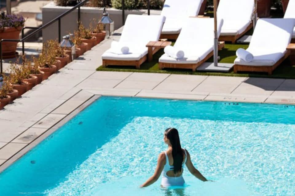 Woman swimming in bright turquoise pool with white loungers and rolled towels poolside