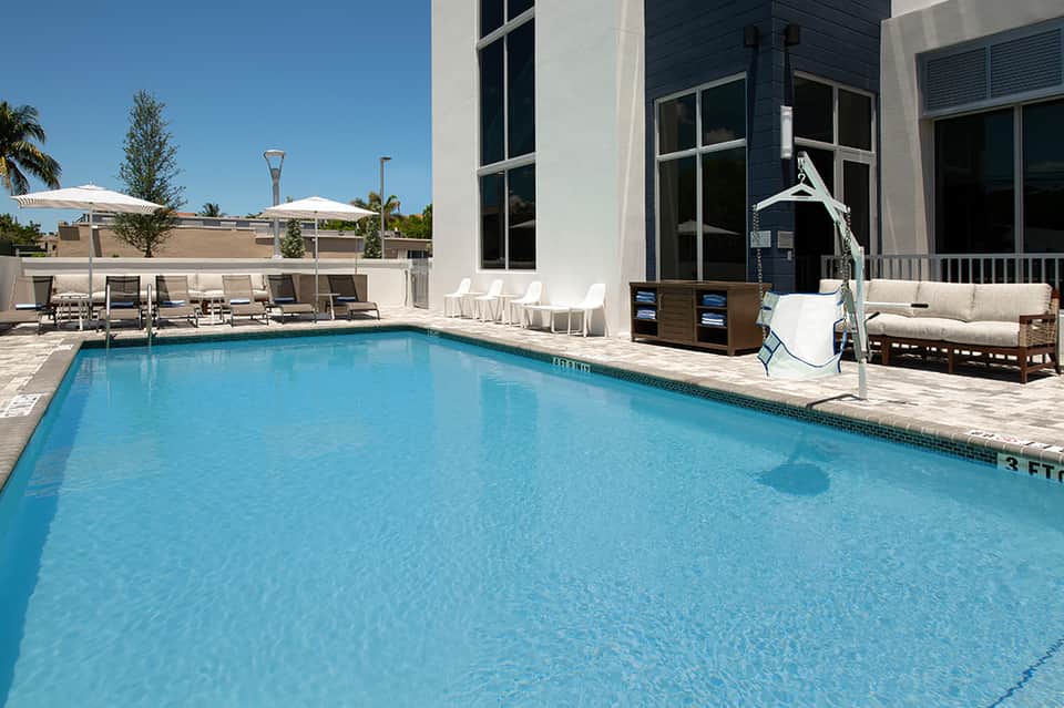Resort swimming pool with lounge chairs, umbrellas, modern building, and clear blue water