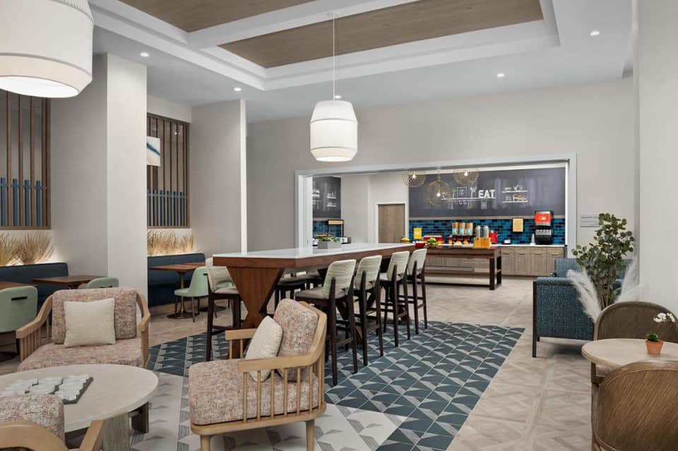 Modern hotel lounge and bar area with wooden furnishings, comfortable seating, and open kitchen setup