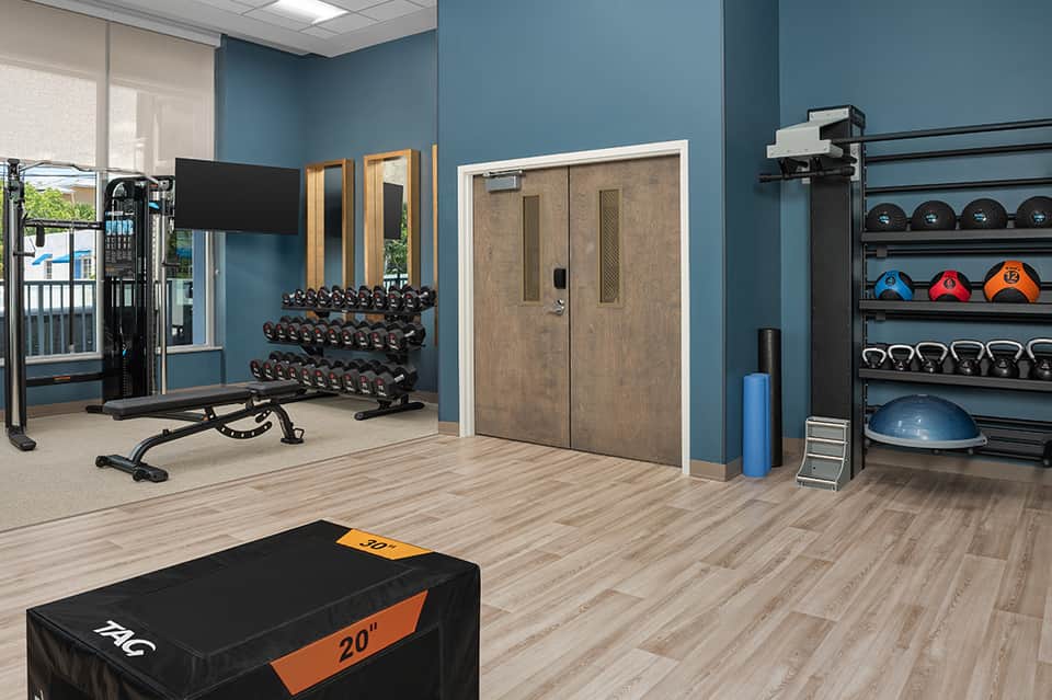 Modern fitness center with blue walls, dumbbells, equipment, and TV mounted on wall