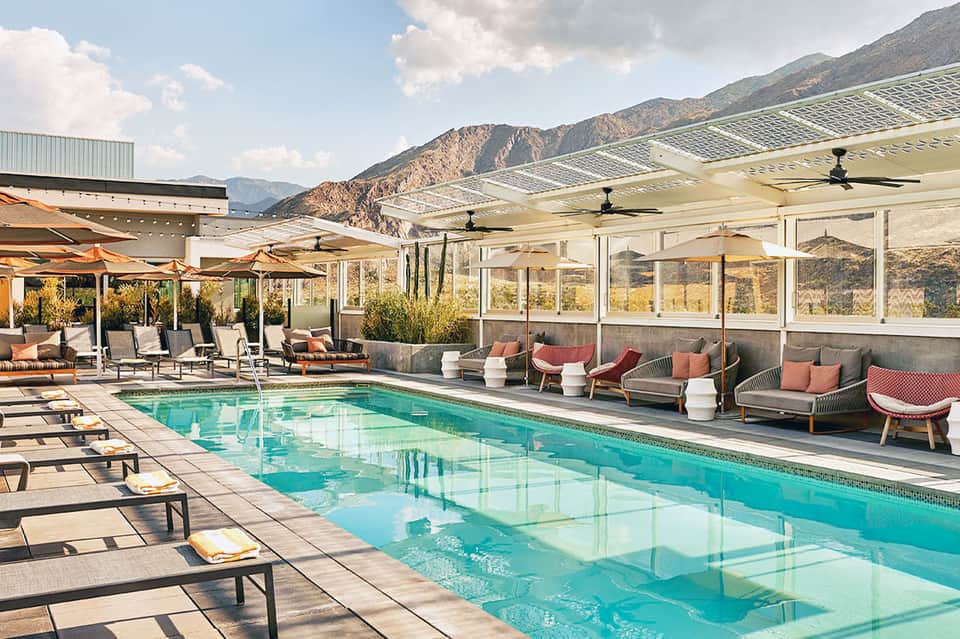 Modern indoor-outdoor pool with retractable glass walls, lounge seating, and mountain landscape