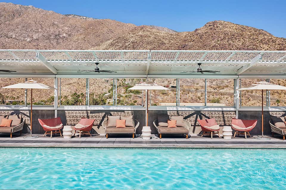 Desert resort pool with red lounge chairs under modern shade structures and mountain views