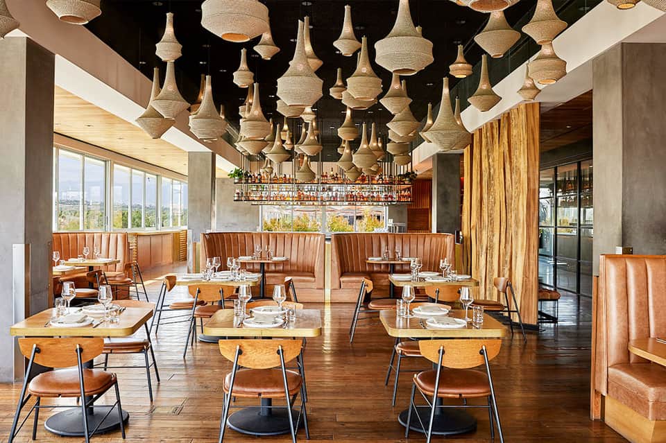 Modern restaurant dining room with woven pendant lights, leather booths, wooden tables, and large windows