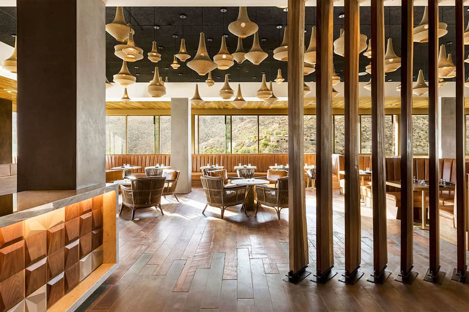 Upscale restaurant interior with brass pendant lights, wooden seating, and scenic outdoor views