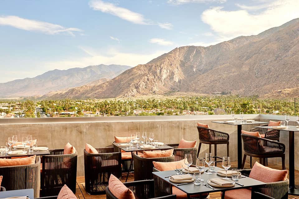 Fine dining terrace with mountain and valley views, woven chairs with orange cushions, place settings