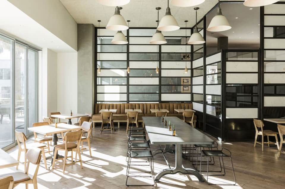 Contemporary restaurant interior with wooden chairs, metal grid partitions, pendant lighting, and large windows