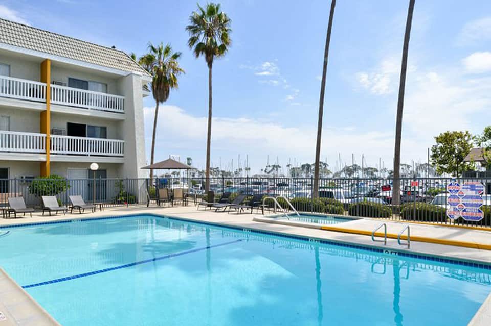 Resort pool with clear blue water, palm trees, modern building, and marina view in background