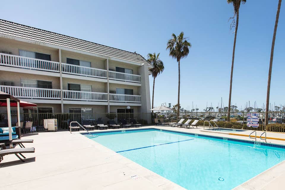 Resort swimming pool with palm trees, white railing, and marina boats visible in distance