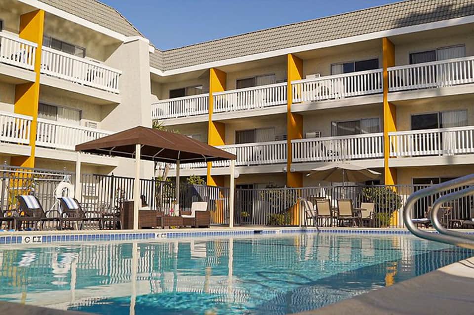 Resort courtyard with curved pool, bright yellow architectural accents, multi-story balconies, umbrellas