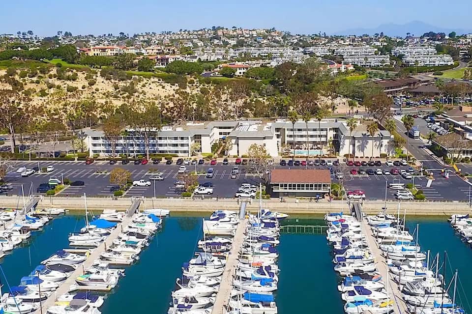 Aerial view of waterfront development with marina, parking lot, and hillside homes