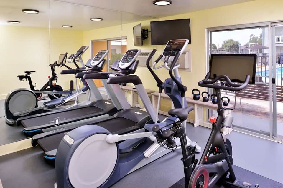 Bright fitness facility with exercise equipment, stationary bikes, and access to pool deck