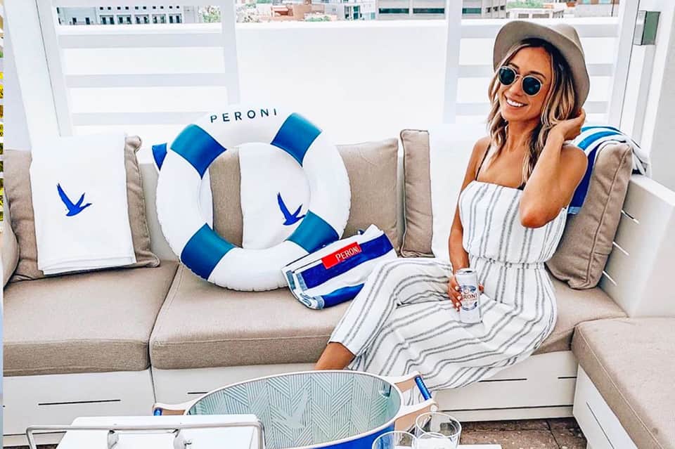 Woman in striped dress on beige sofa with Peroni branded pillows and life ring at luxury lounge