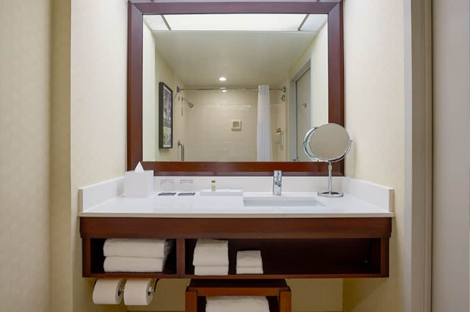 Luxury bathroom vanity with large framed mirror, white sink, wood trim, and rolled towels below