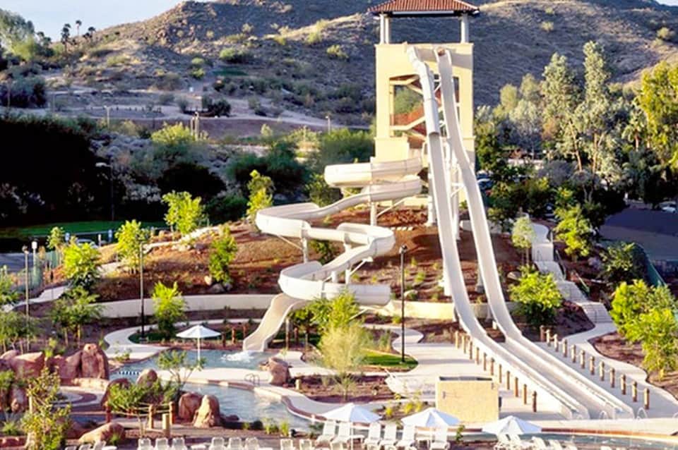 Spiral water slide tower at resort water park with surrounding landscaping and hills in background