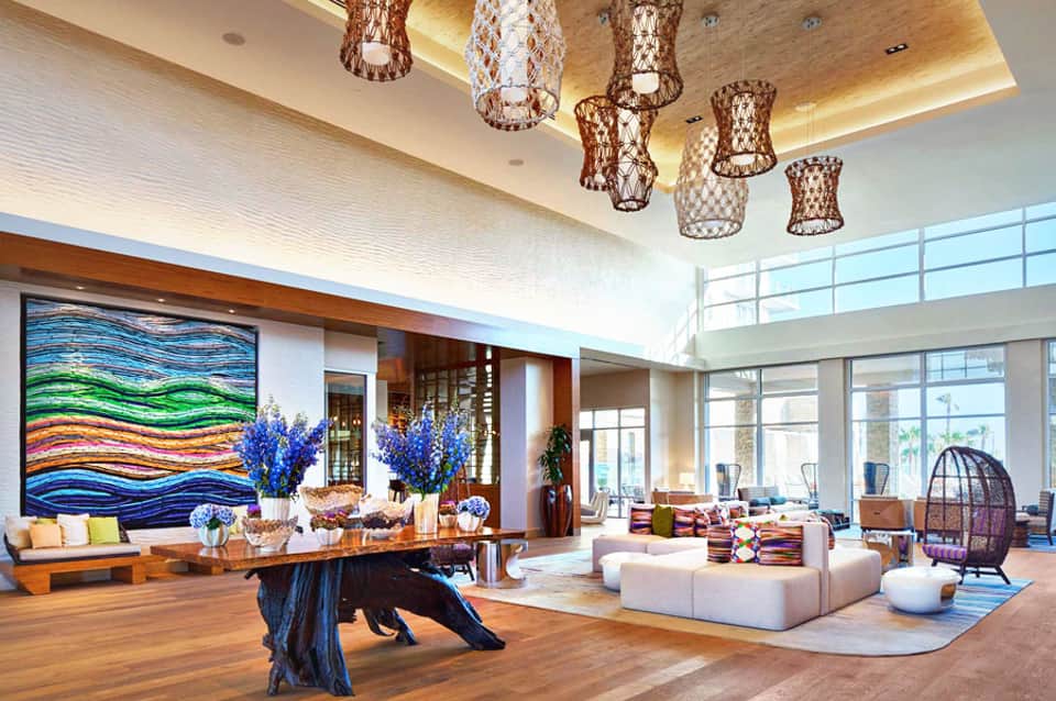 Luxurious hotel lobby with colorful wave artwork, hanging woven light fixtures, wooden furniture, and modern seating areas
